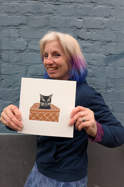 print of a Black cat in a basket held by Liz