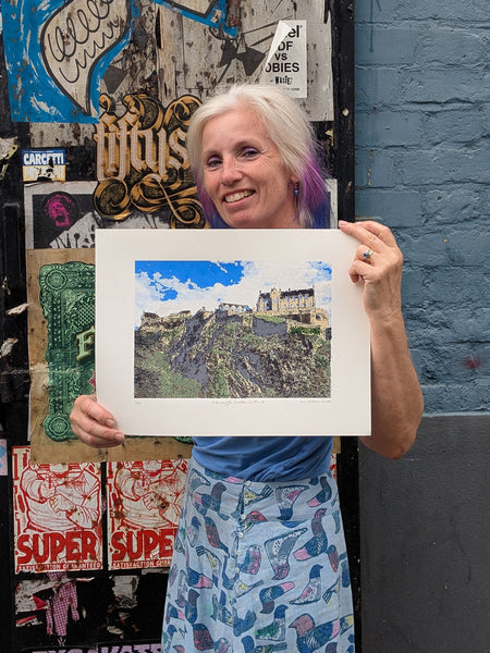 Liz holding a framed picture of a castle against a colorful wall.
