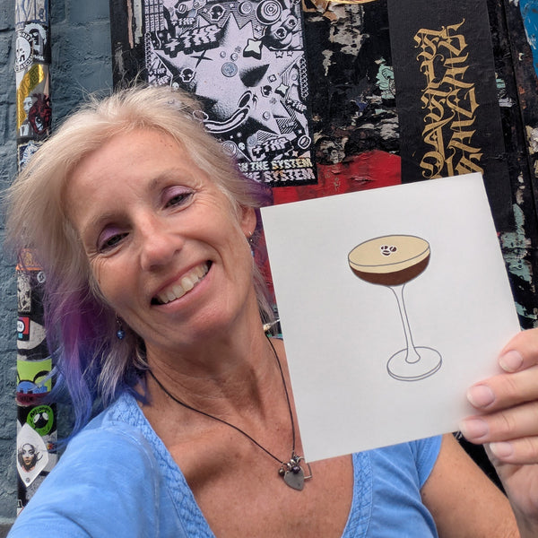 A print of a coupe glass filled with a layered drink, topped with a light beige layer and dark brown espresso layer, with three coffee beans on top held by Liz