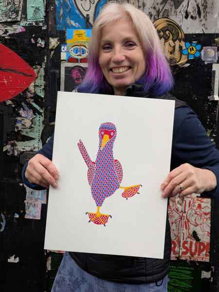 Liz holding a Colourful bird print with red, blue and purple pattern with hearts on red feet