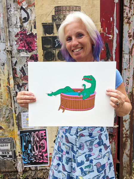 Liz holding the Dinosaur sitting in a Hot tub with a cocktail screen print