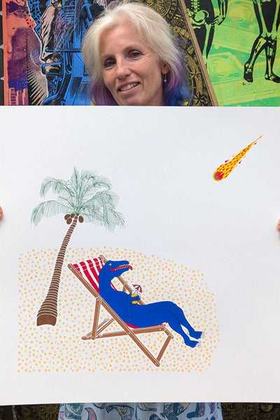 a dinosaur relaxing in a deckchair on a desert island as a meteor hurtles towards him print held by Liz