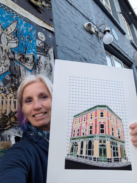 A screen print of the Starting Gate pub  with a racing horse background held by Liz