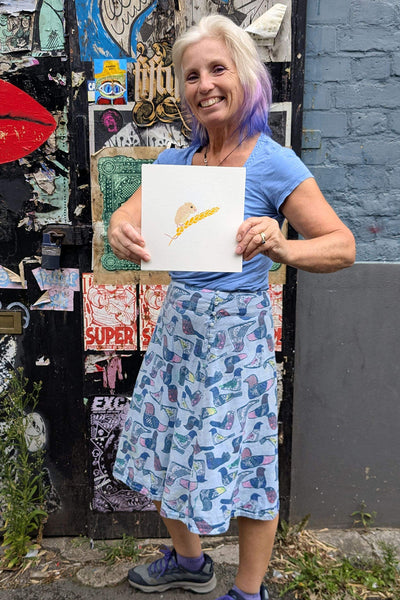 Liz holding a print of a field mouse on a stalk of wheat