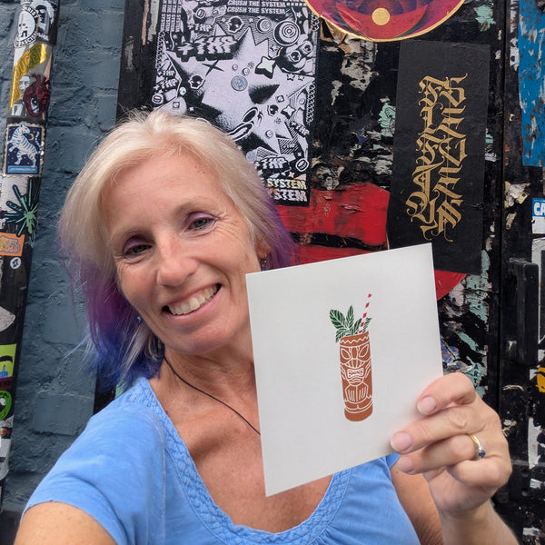 A minimalist print of a tiki drink called a Zombie by artist Liz Whitman Smith. The print features a terracotta-coloured tiki mug with white line art, green mint leaves, and a red-and-white striped straw held by Liz